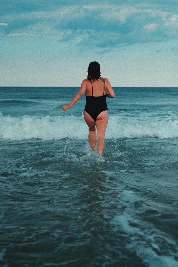 A woman in a black swimsuit runs into the ocean waves on a summer day.